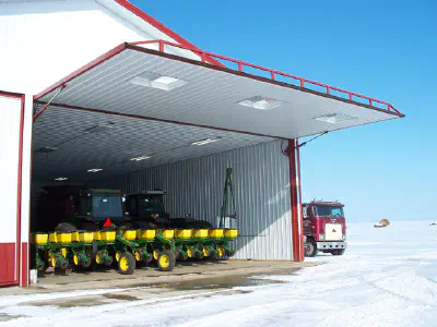 Outside view of a large garage with the door open showing farming tractors
